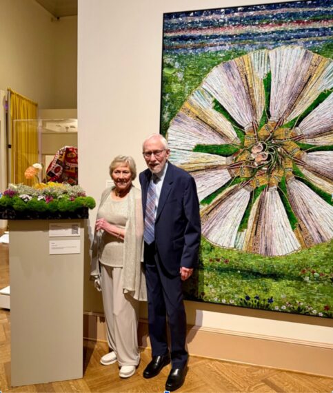 Older woman and man standing in front of a piece of art hanging on the wall and a floral interpretation