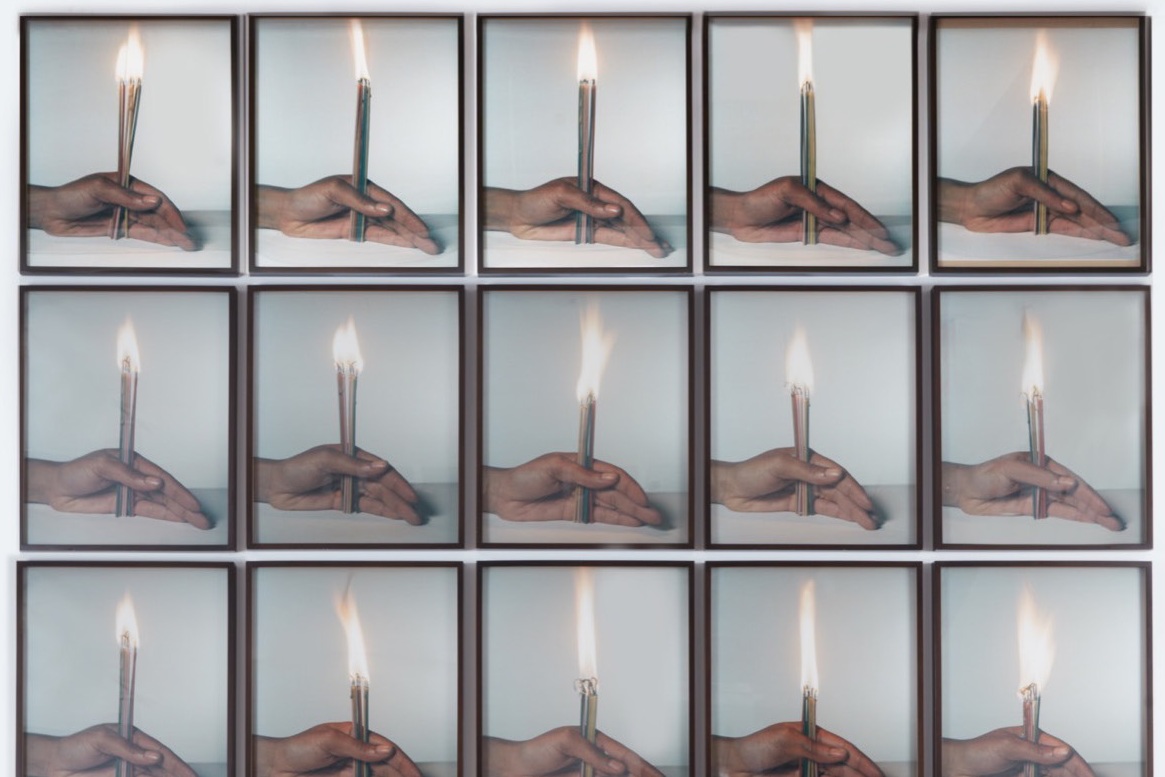 The image shows a grid composed of framed photographs arranged in five rows and five columns, totaling 25 individual images. Each photograph features a hand holding a lit candle against a neutral background. The candle is vertically positioned, with the flame clearly visible at the top.