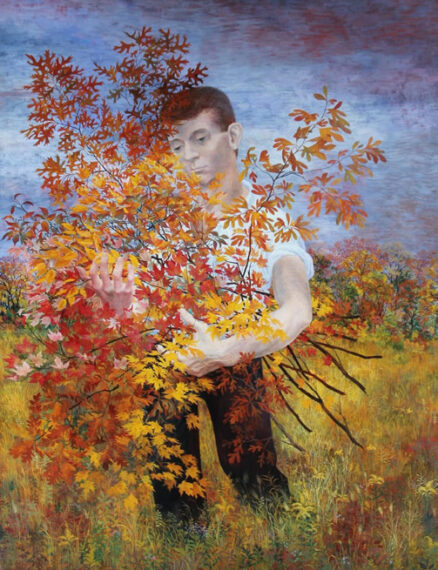 The image shows a person standing in a field filled with autumn-colored plants. They are partially obscured by a vibrant bush with leaves in various shades of red, orange, and yellow.