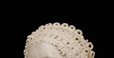 A marble sculpture showcasing the top portion of a head, prominently featuring an intricately detailed hairstyle.