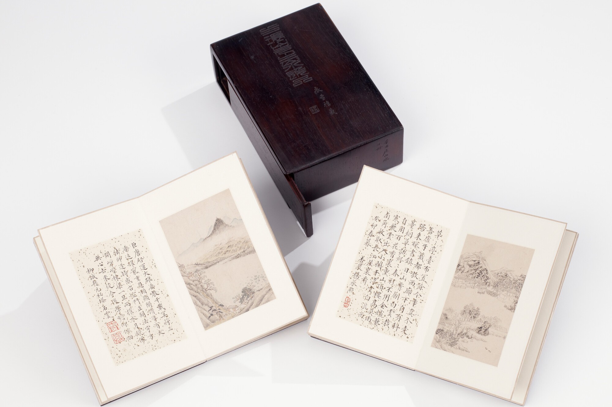 Two open books with Chinese calligraphy and drawings next to a wooden box.
