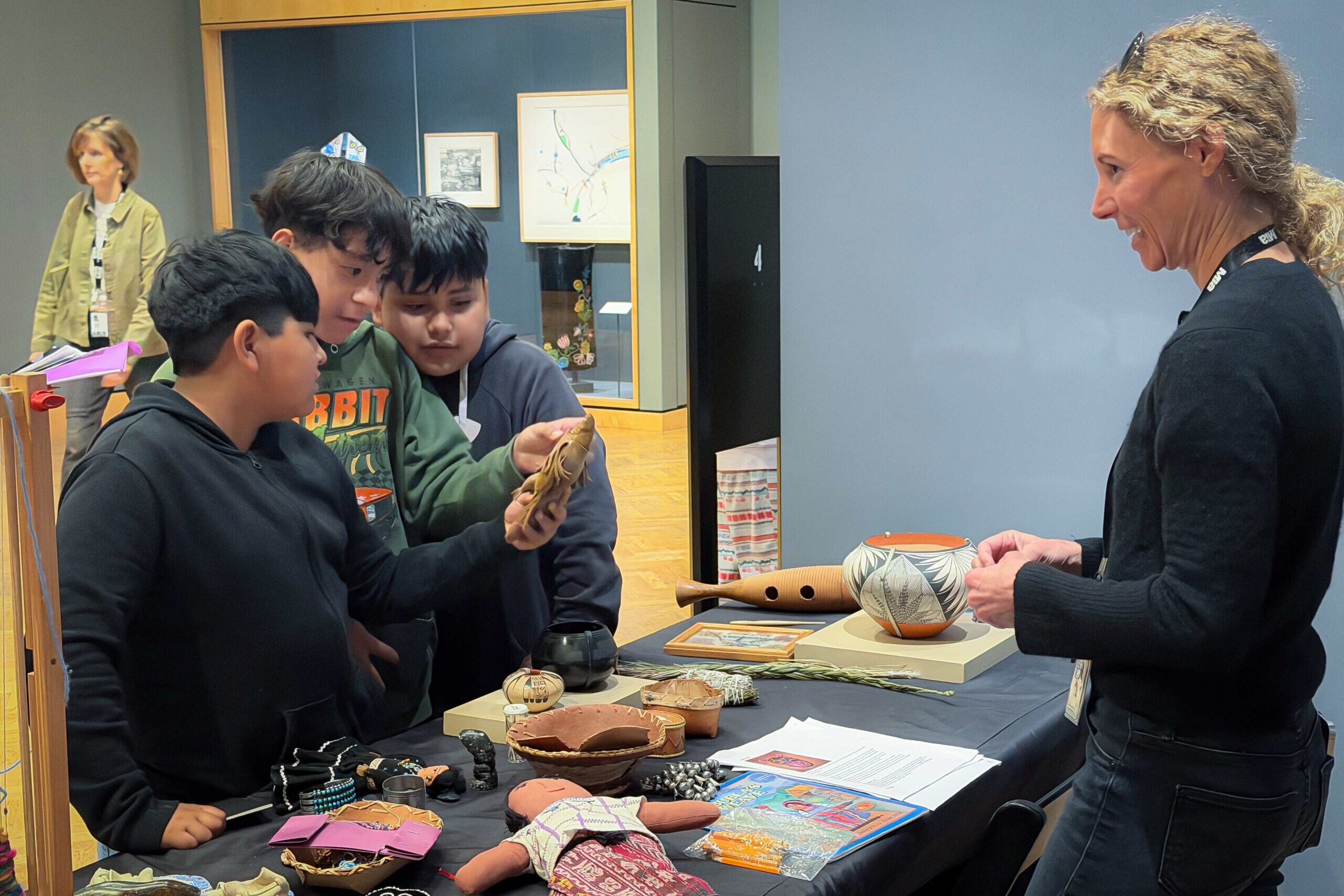Group of boys examining objects on a table with a woman nearby.