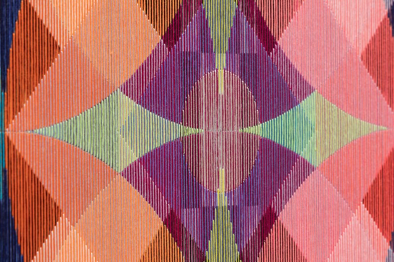 The image features a colorful geometric pattern composed of various intersecting shapes featuring shades of orange, pink, green, purple, and blue.
