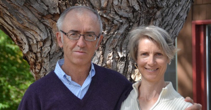 The image shows two people standing closely together by a large, textured tree trunk.