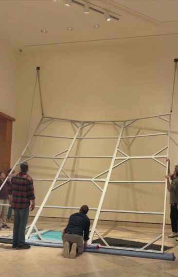 Large metal frame being installed in a gallery space.