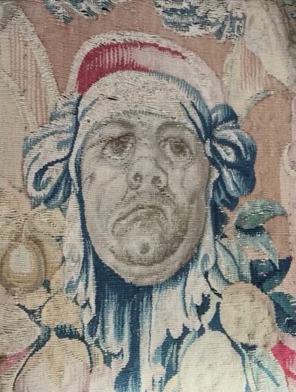 Detailed section of a tapestry with a face wearing a headscarf adorned with bows.