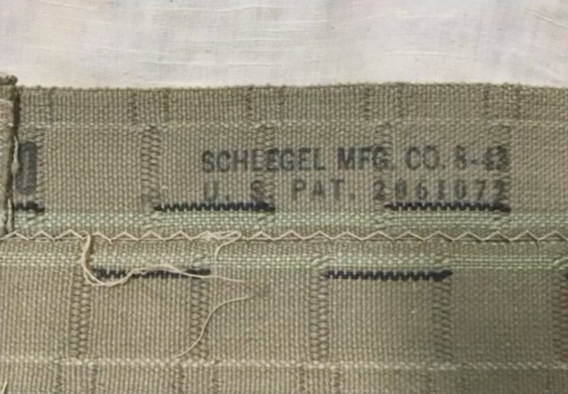 The image shows a section of green fabric with visible stitching details. The fabric features horizontal stitching lines and vertical seam patterns. There's black printed text on the fabric that reads 'SCHLEGEL MFG CO. 8-43 U.S. PAT. 2061072'.