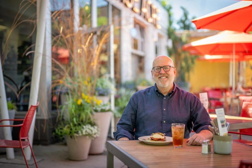 Man sitting at outdoor cafe table with food and drink.