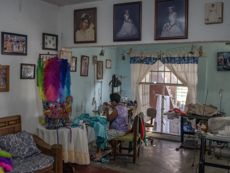A person sewing in a room with multicolored feathers and portraits on the wall.