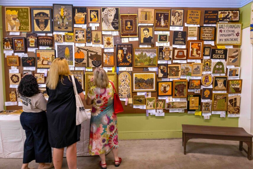 Photo of three people viewing a wall of framed artwork.