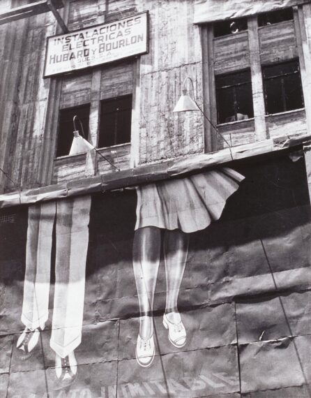 The image shows a black-and-white photo of a vintage building facade with a sign and a painted mural.