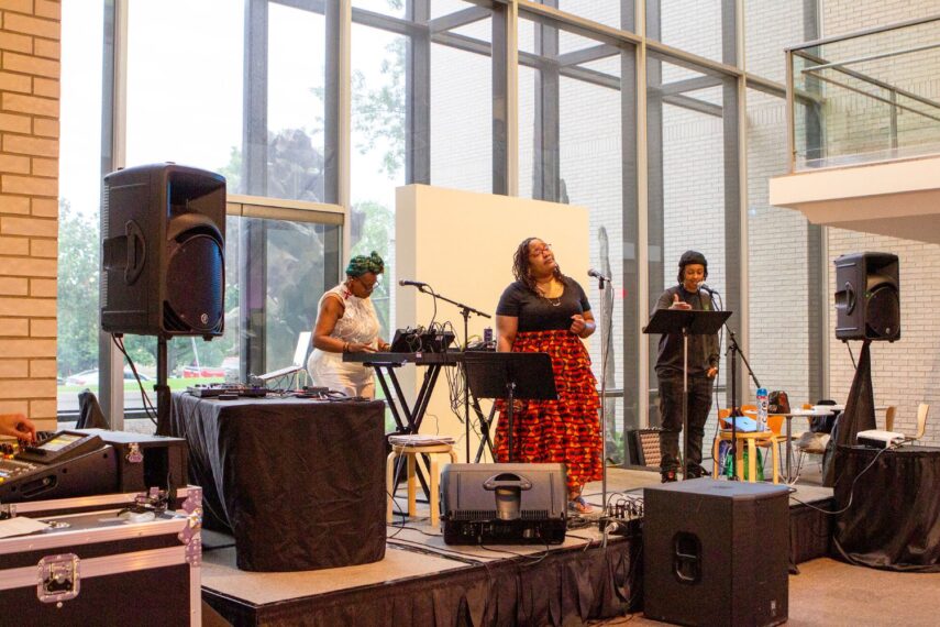 Three performers on a stage with musical equipment.