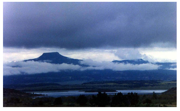 Photo of a mountain landscape with clouds and water in foreground.