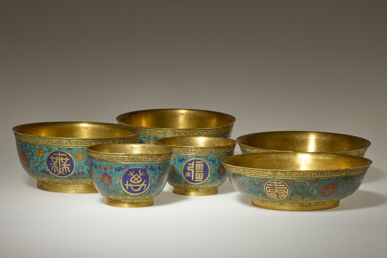 The image features five decorative bowls arranged close together. They are made of gold and have intricate designs along the outer surface. The designs include blue and gold patterns, with some red and green floral motifs.