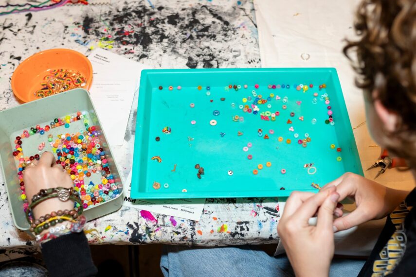 The image shows people picking colorful beads from two trays on a craft table.