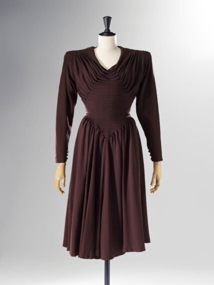 The image shows a mannequin dressed in a vintage-style, long-sleeved brown dress.