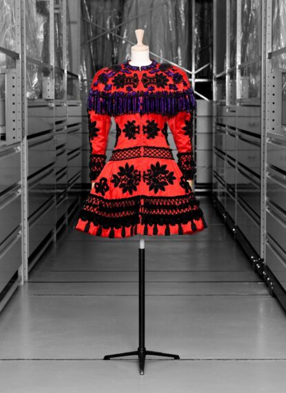 Red dress with black and purple floral patterns and fringe on a mannequin.