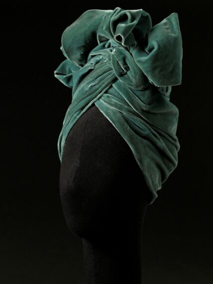 The image shows a mannequin head wearing an intricately wrapped green velvet turban.