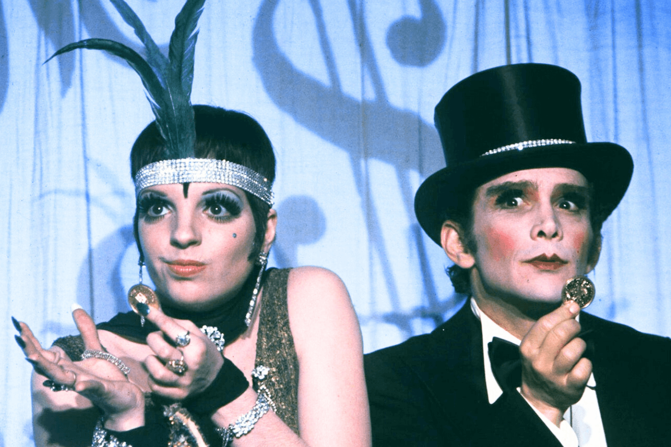 Two people in theatrical costumes and makeup holding coins.
