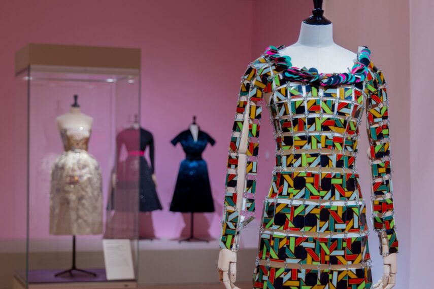 Colorful geometric long-sleeved mini dress on a mannequin in pink room with three other dresses displayed in the background.