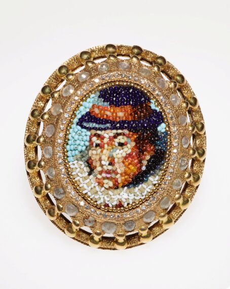 Ornate brooch with a beaded portrait in the center.