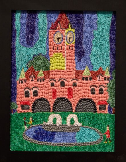 Bead art of a tall pink building with towers, arches, and a fountain.