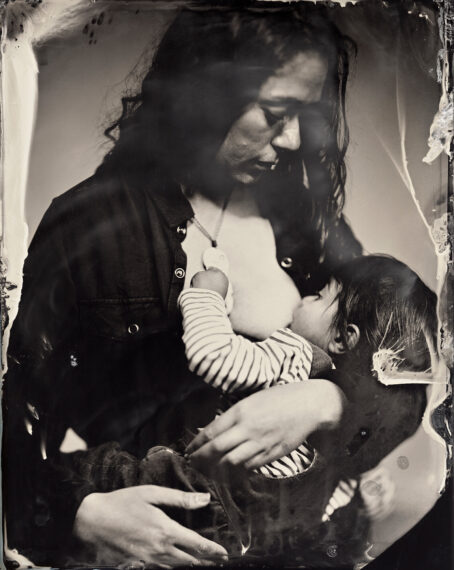 Black-and-white photograph of a woman sitting and breastfeeding a child.